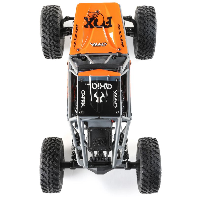 Gray and orange Axial 1/18 UTB18 Capra 4WD RTR trail buggy on rugged terrain, showcasing its compact off-road design.