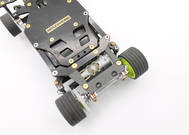 Reflex Racing RX28A-01 RC car rear brass and carbon fiber lower pod plate showing detailed metal and carbon fiber components.