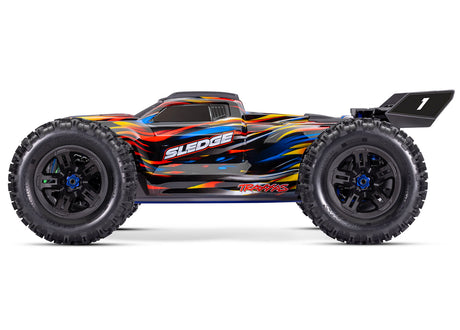 Traxxas 1/8 Sledge belted RC truck with blue accents and rugged tires, shown from the side view.