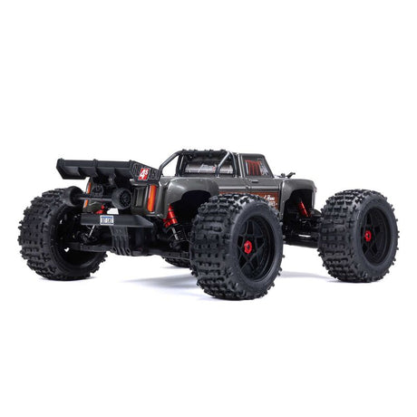 ARRMA Outcast 4X4 4S 1/10th scale 4WD stunt truck shown on rugged terrain with aggressive tires and vibrant orange body.