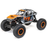 Gray and orange Axial 1/18 UTB18 Capra 4WD RTR trail buggy on rugged terrain, showcasing detailed off-road design.