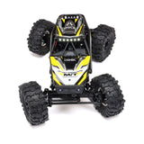 Axial 1/18 Capra 4WS brushed rock crawler showing detailed chassis and four-wheel steering in a rugged outdoor setting.