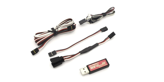Kyosho I.C.S USB Adaptor HS 82083 connected to a compressor, showing a compact, black electronic adapter with USB port for RC tools.